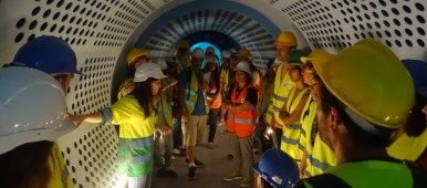Grupo de personas con chalecos reflectantes y cascos de obra en un pasillo abovedado estilo túnel